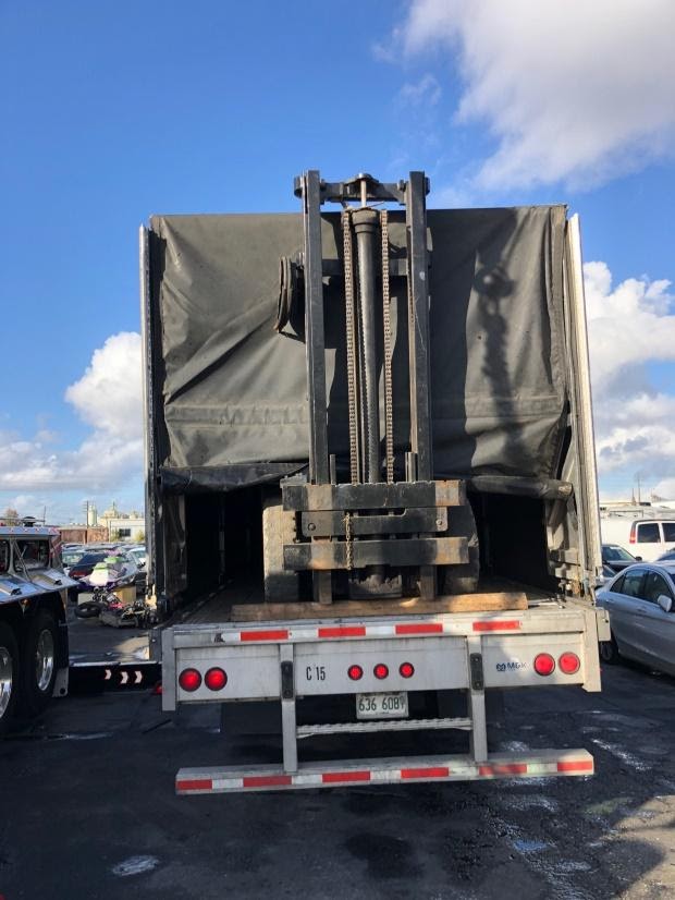 Truck carrying a forklift on a trailer.