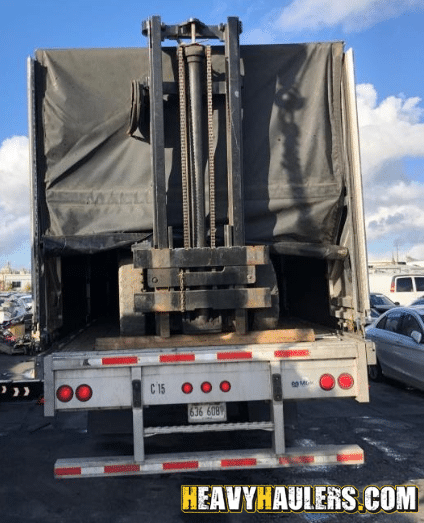 Truck transporting a forklift on a conestoga trailer.