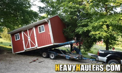 Moving a red storage shed on a trailer.